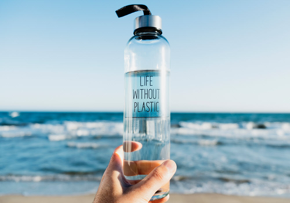 Person at the beach holding a reusable water bottle. 