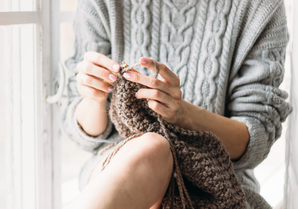 Woman practices knitting as a new hobby in her apartment home.