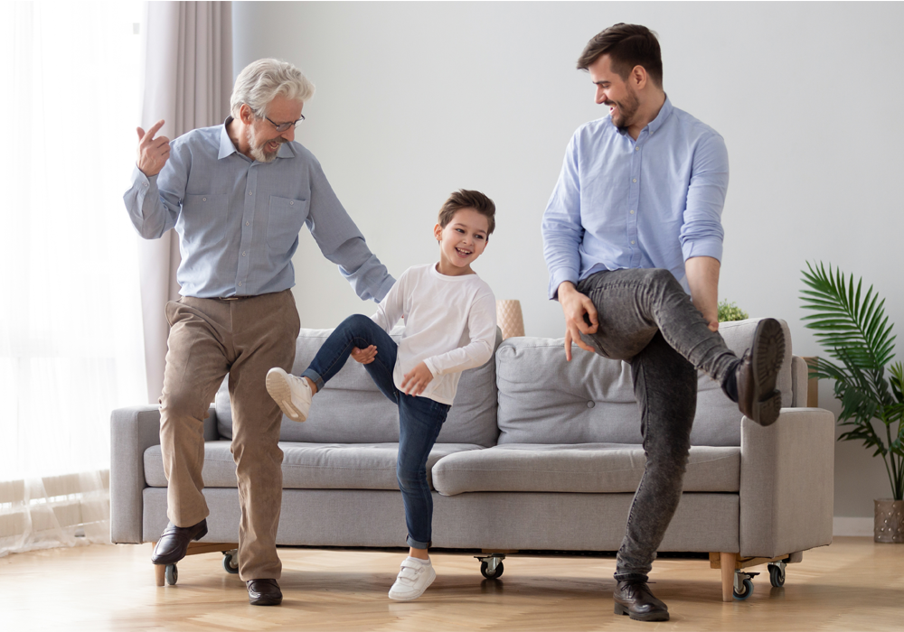 Grandfather, father, and son dancing together in their West Coast apartment home living room.