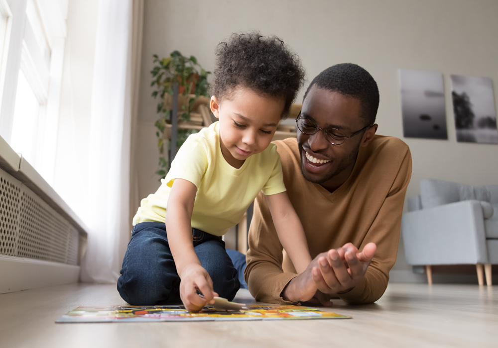  Father and son working on a puzzle on the hardwood-style flooring of an apartment living room.