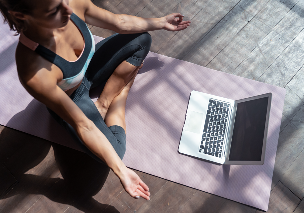 Woman following an online virtual yoga mediation class on her laptop.