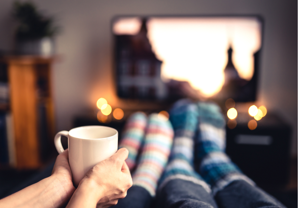 Aesthetic image of a couples' feet and a mug with a tv in the background.