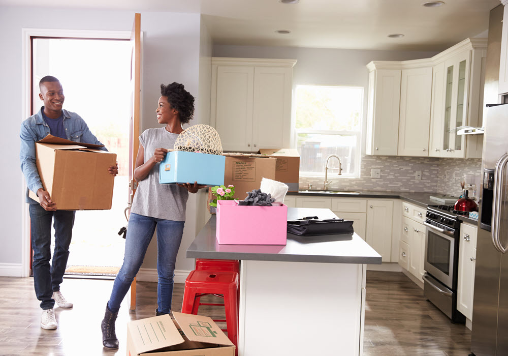Couple carrying moving boxes into an apartment.