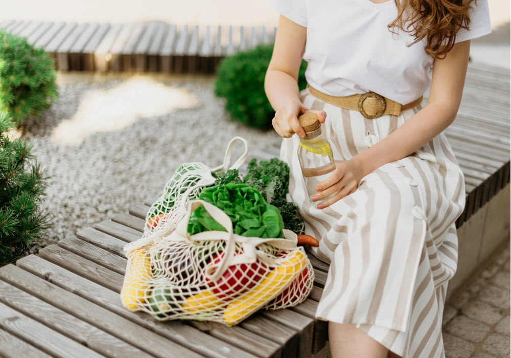 Woman sitting next to a eco-friendly bag full of produce.