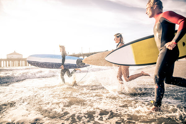 Surfers running into water.