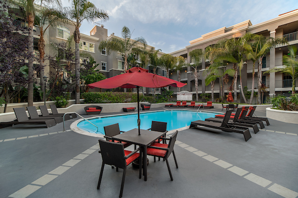Outdoor swimming pool area with lounge seating and tables with umbrellas.