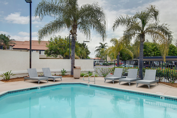 Outdoor swimming pool area with lounge seating surrounded by plants.