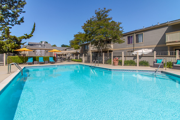 Outdoor swimming pool with sundeck, lounge chairs, and umbrellas.