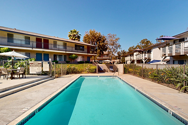 Outdoor swimming pool surrounded by tables, chairs, and umbrellas.